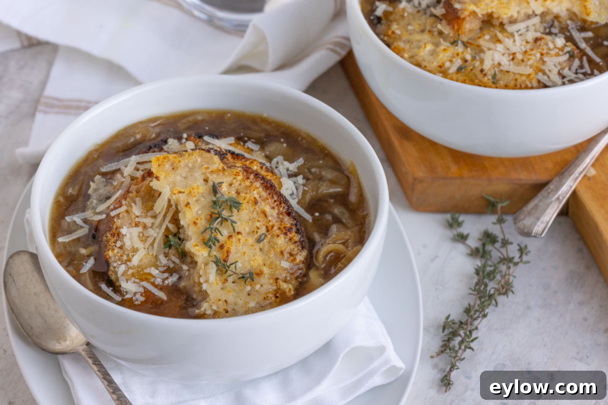 Effortless French Onion Soup 5 Two white bowls of golden French onion soup with crusty cheesy croutons and fresh thyme garnish, ready to serve.