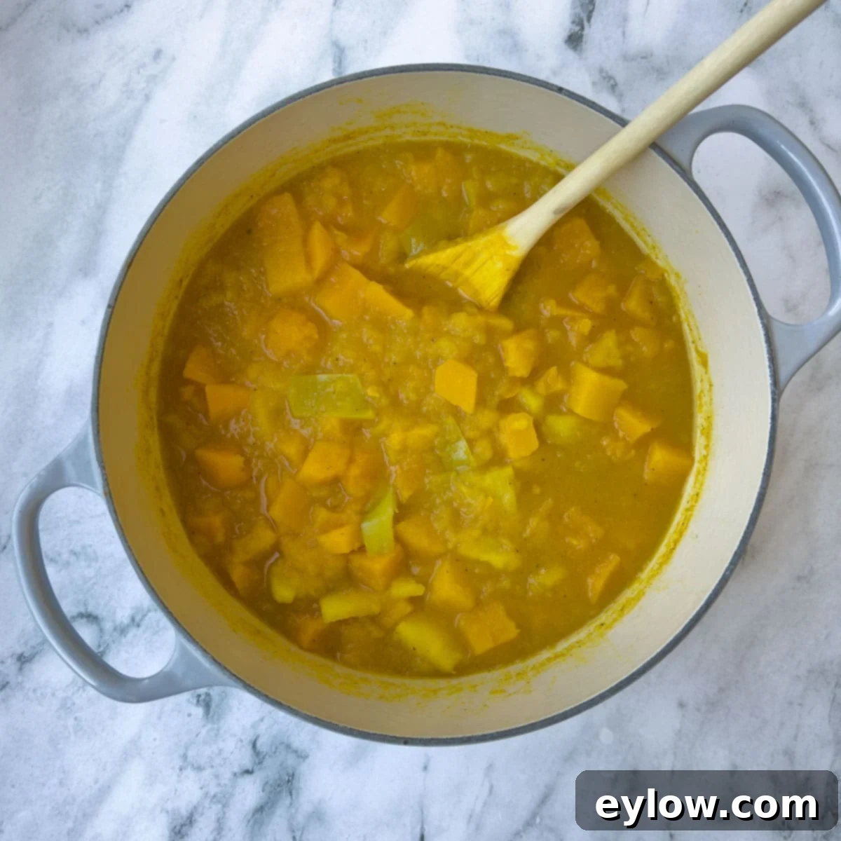Velvety Butternut Apple Comfort Soup 6 A close-up of colorful butternut apple soup, already cooked and softened, in a pot on a kitchen counter, ready for blending.