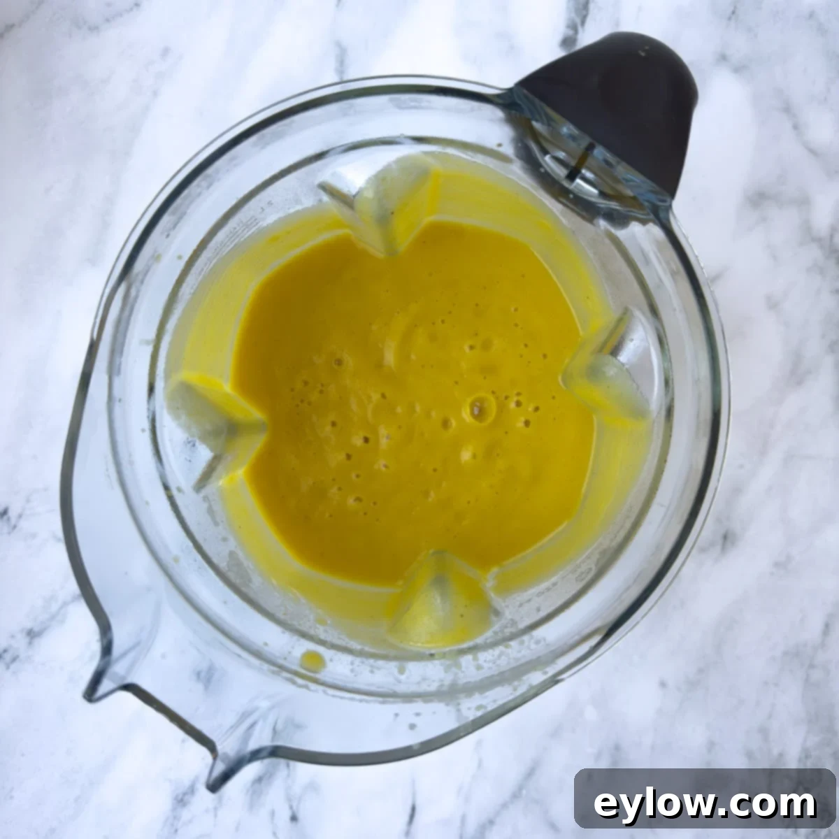 Velvety Butternut Apple Comfort Soup 7 Bright orange pureed butternut apple soup inside a blender container, showing its smooth and creamy texture.