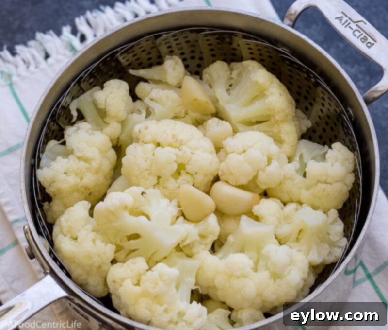 Cauliflower florets in a steamer rack in a pot.
