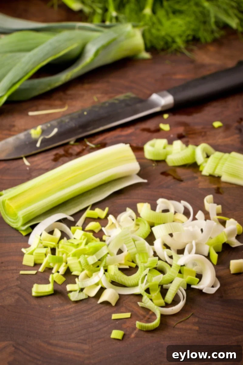 A chef chopping leeks into half-moon shapes on a rustic walnut cutting board.