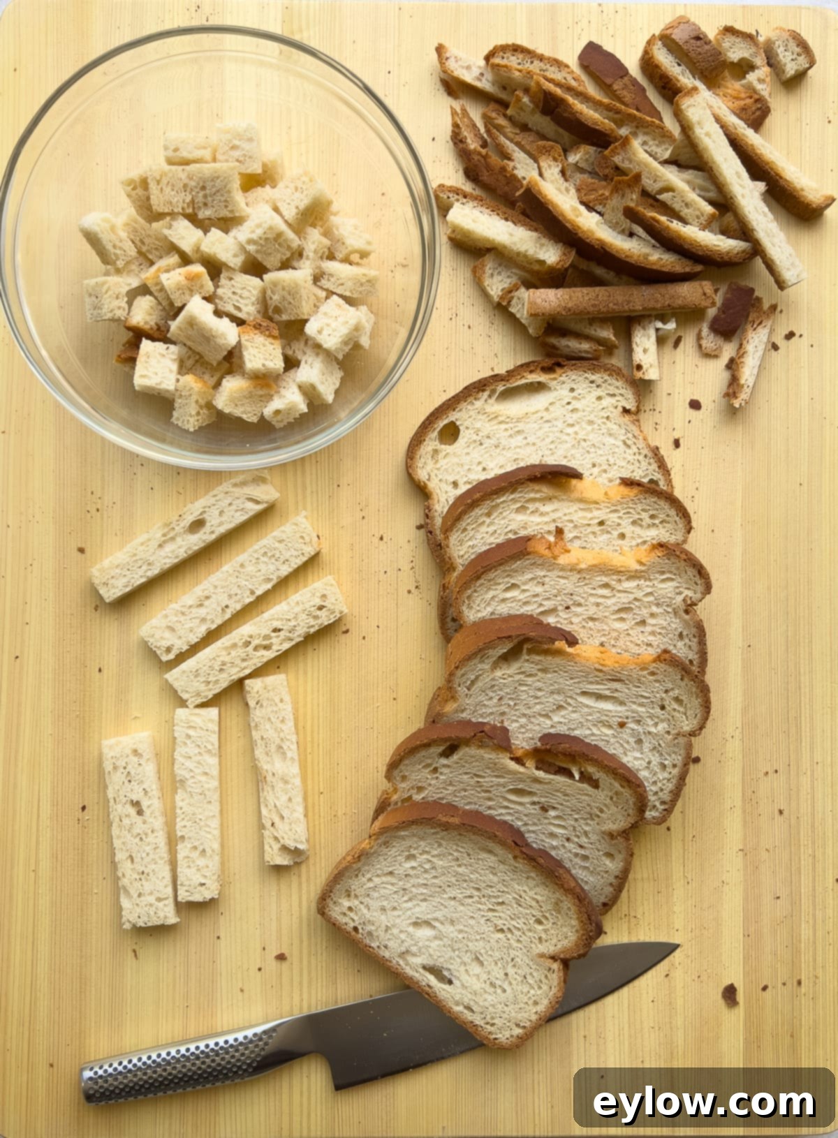 A person cutting gluten-free bread into cubes for stuffing on a wooden cutting board.