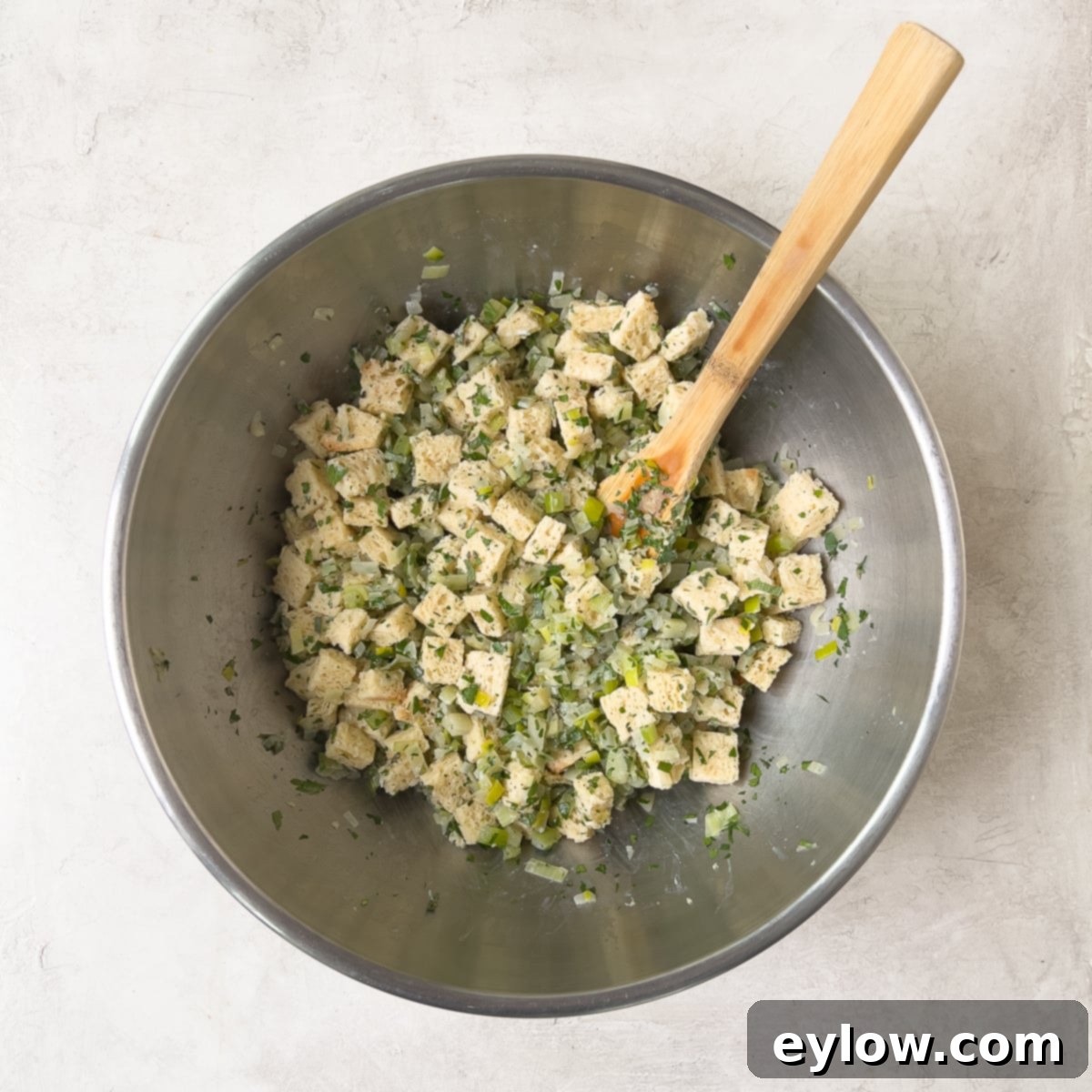 A large mixing bowl filled with dried bread cubes, sautéed vegetables, and fresh herbs, ready for the liquid.