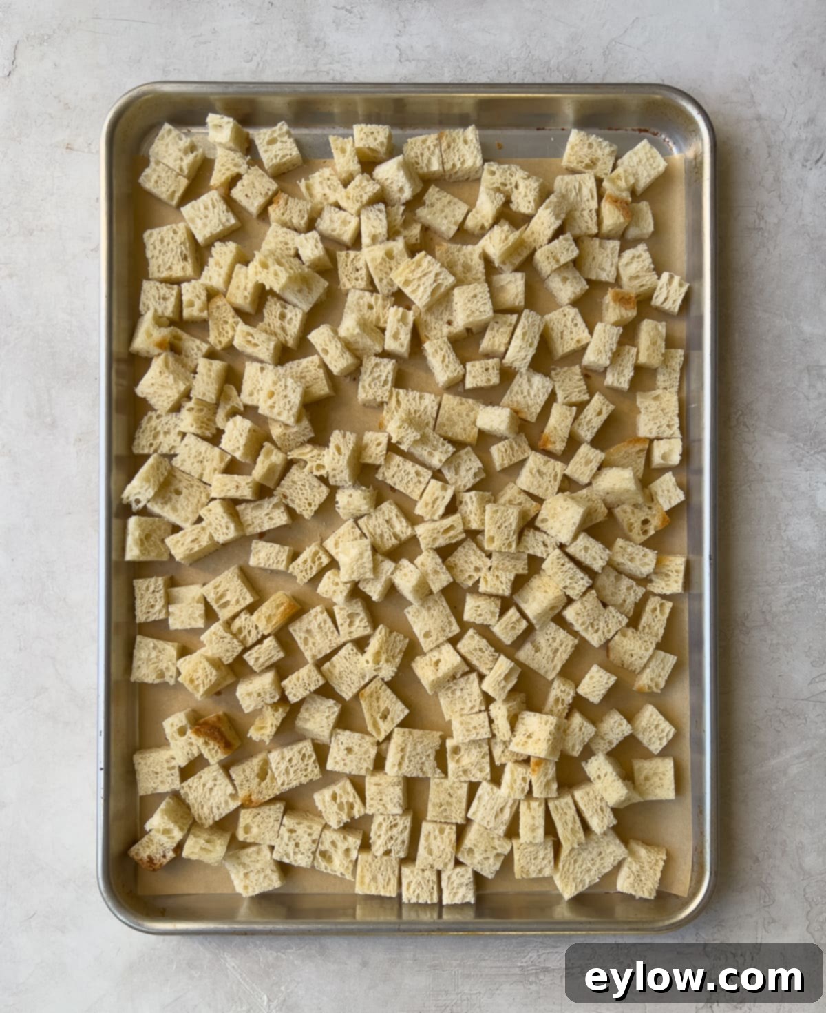 Uniformly cut gluten-free bread cubes spread on a baking sheet to dry for turkey dressing.