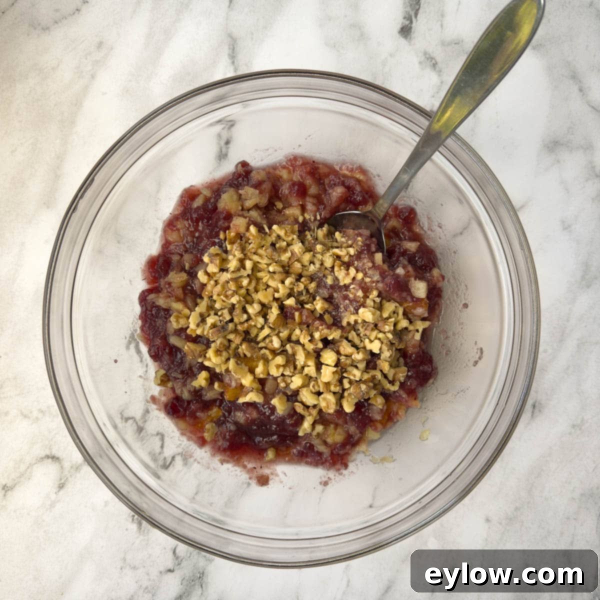 Fruit for a cranberry salad combined with chopped walnuts in a glass bowl.
