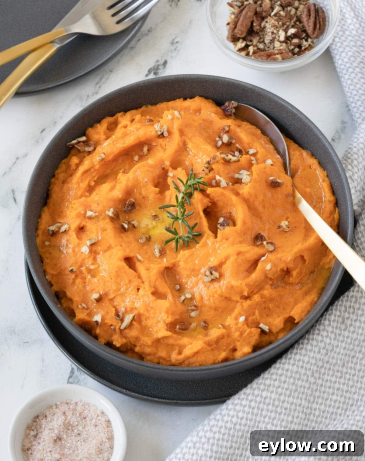 A bowl of bright orange whipped sweet potatoes in a gray bowl with chopped pecans for garnish.
