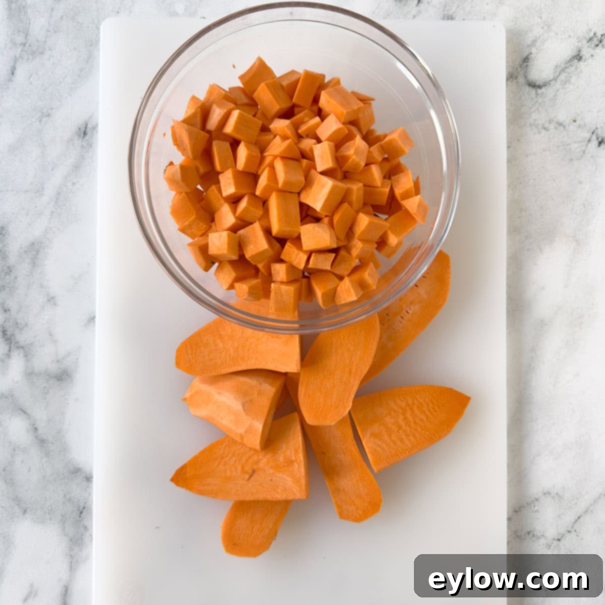 Cubed sweet potatoes in a glass bowl with wedges on the cutting board.