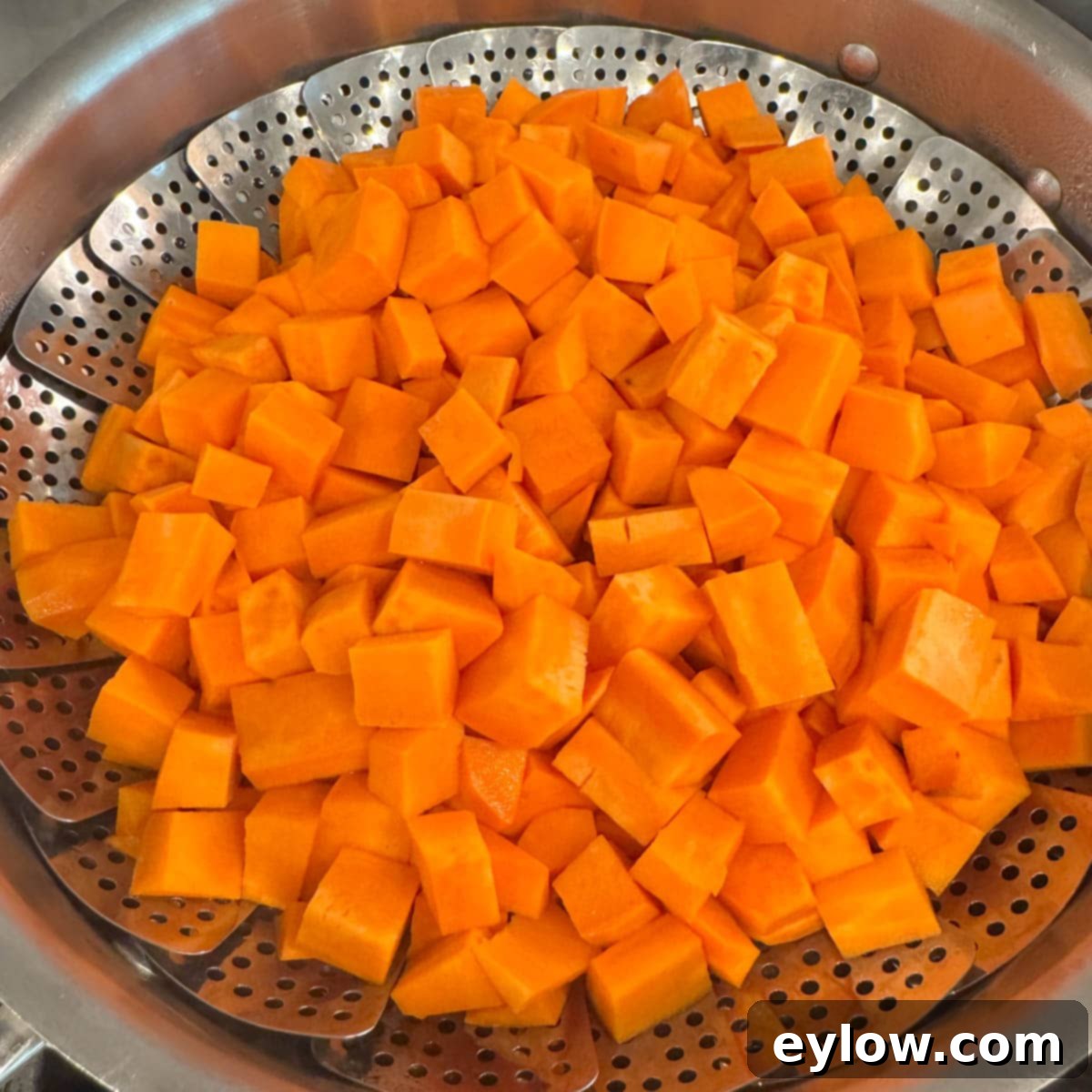 A steamer basket filled with diced orange sweet potatoes. 