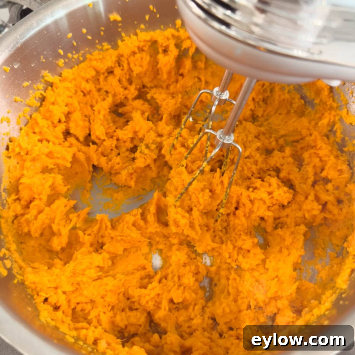 Whipping sweet potatoes with a hand mixer until smooth in the cooking pot. 