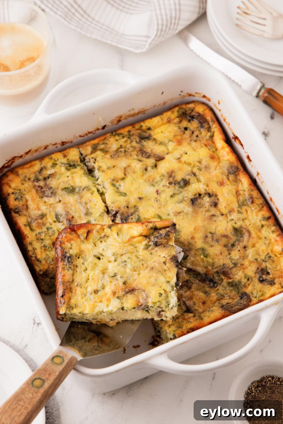 A golden baked breakfast casserole with eggs, mushrooms, broccoli, and quinoa in a white baking dish.