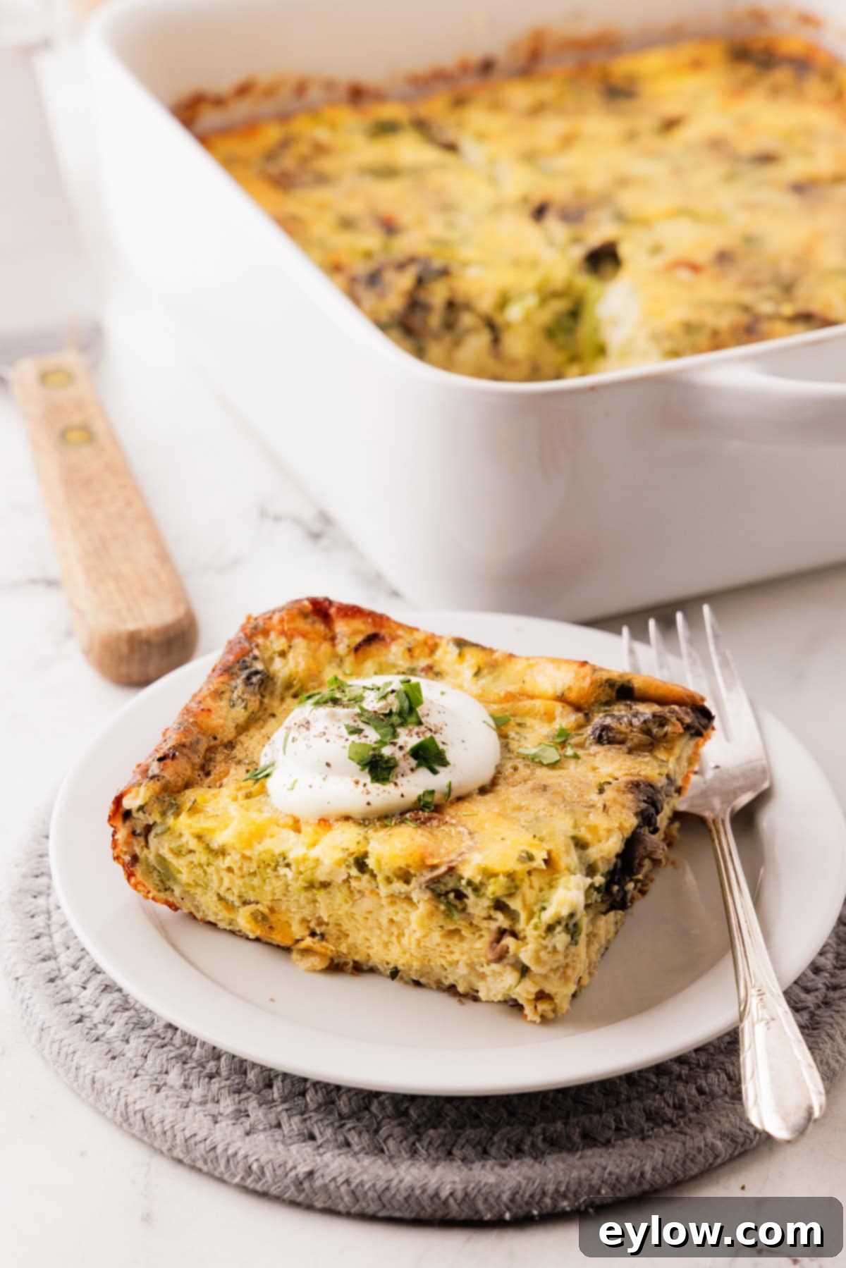 A piece of gluten free breakfast baked egg casserole on a white plate with a silver fork.