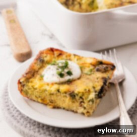 A piece of golden baked breakfast casserole with eggs on a plate with a fork and dollop of sour cream on top.