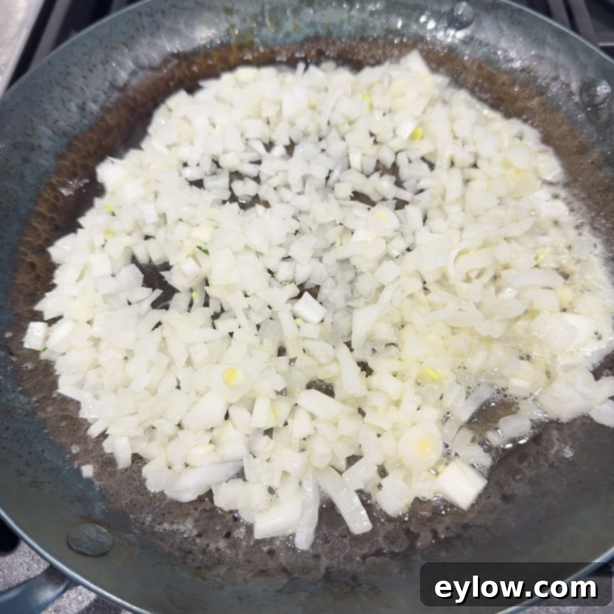 White onions sauteeing a a black steel pan.