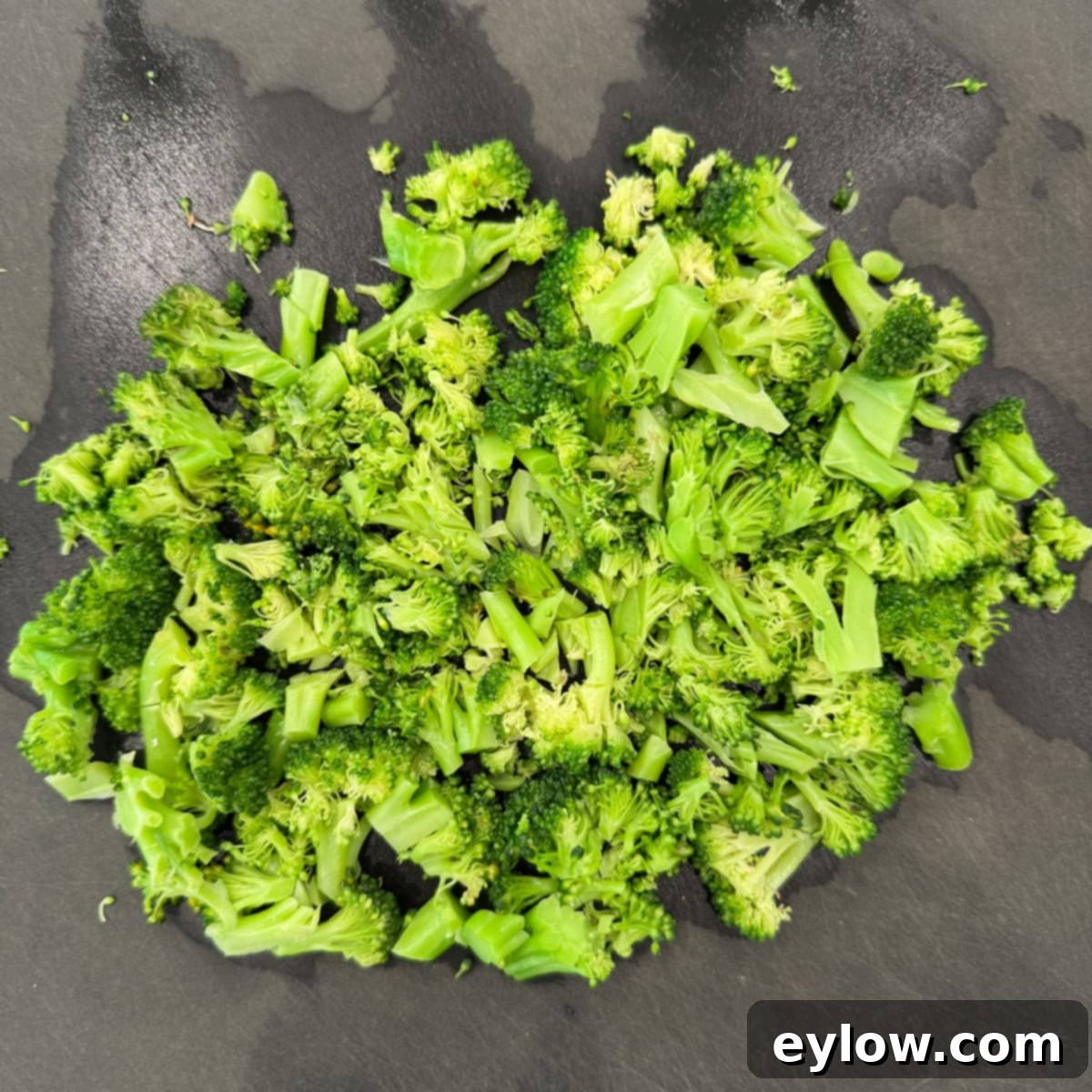 Cooked chopped broccoli on a black cutting board.