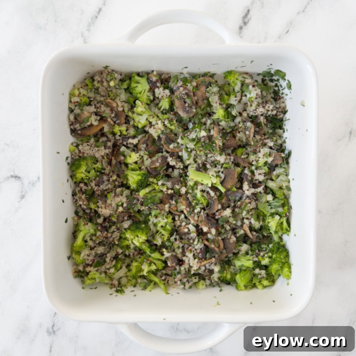 A white baking dish filled with broccoli, mushroom, quinoa, and herbs for a breakfast casserole.