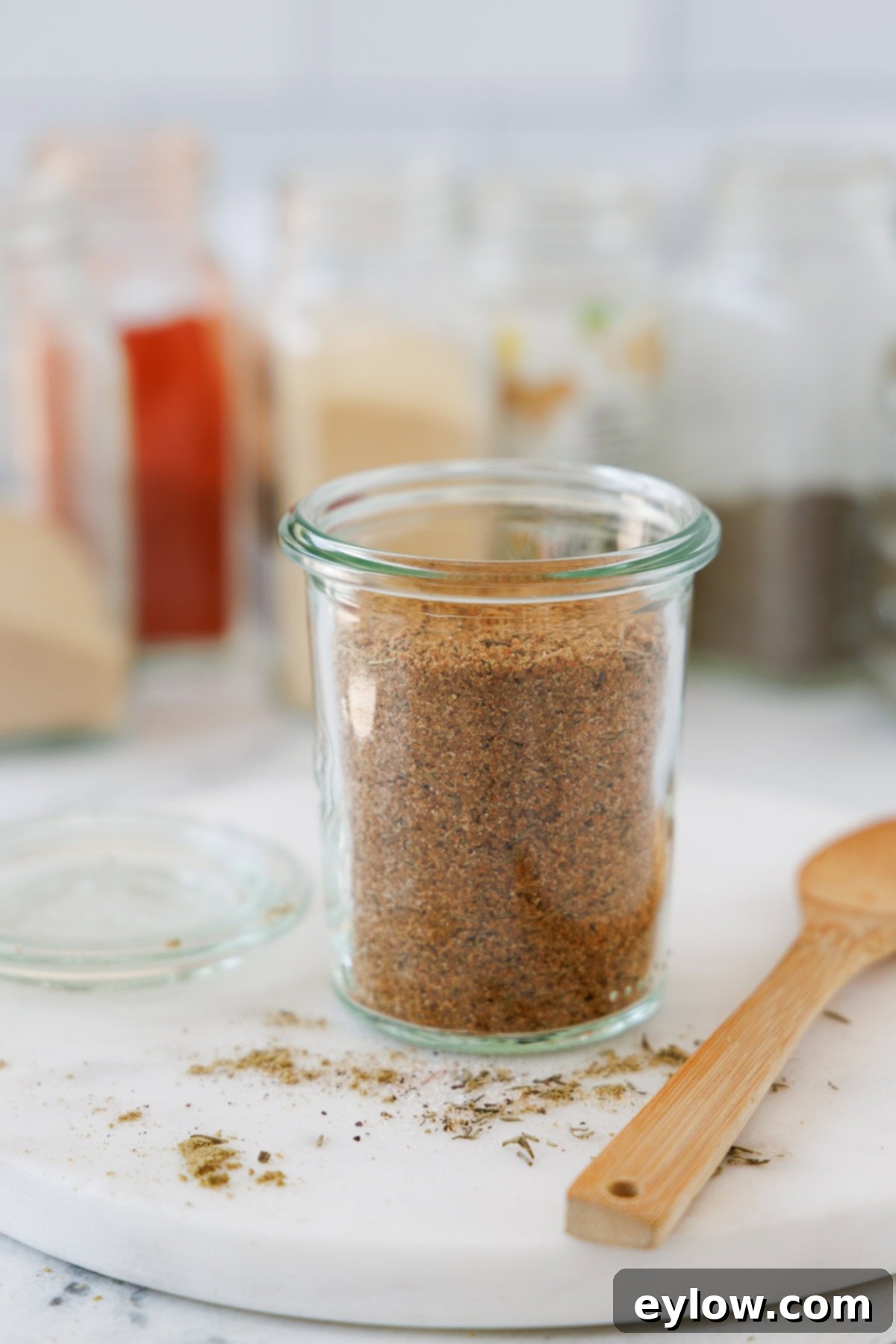 A jar of colorful turkey seasoning blend with a wooden spoon, spices jars in the back.