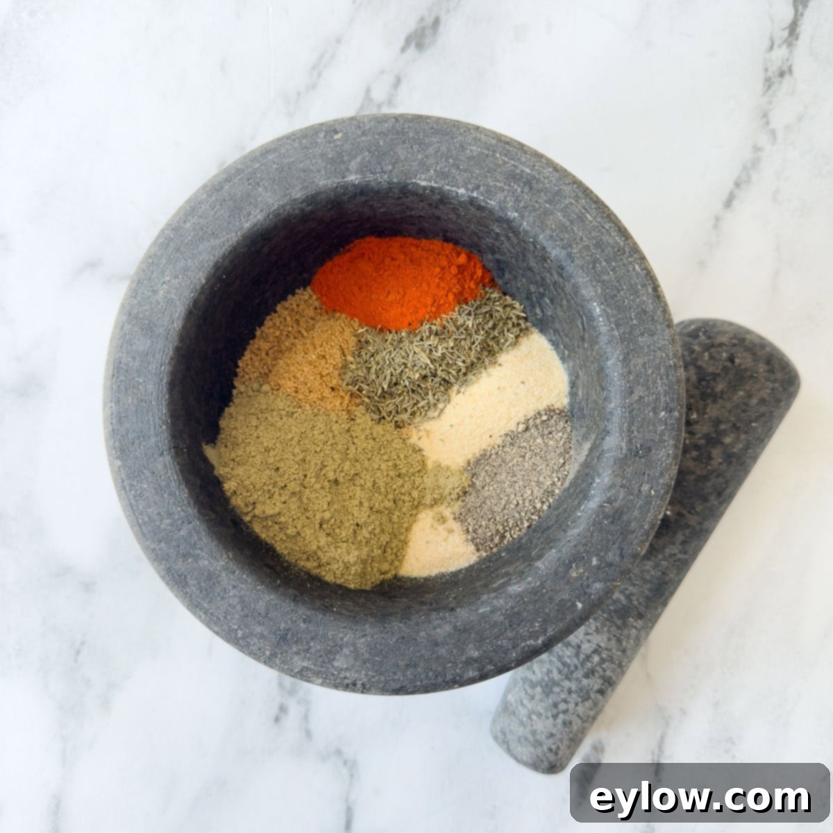 Brightly colored herbs and spices in the bowl of a gray mortar for blending. 