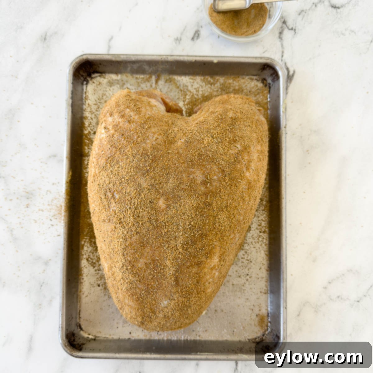 Turkey breast covered in dry rub seasoning on a baking tray.