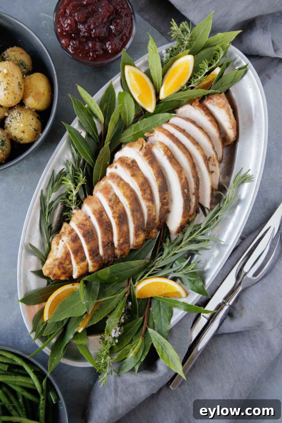 A sliced smoked turkey breast on a pewter platter with bay leaves and orange wedges.