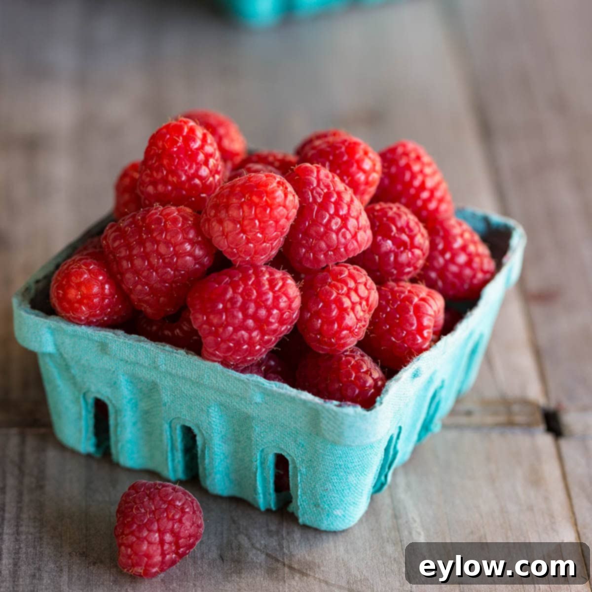 Raspberry Refresher: A Guilt-Free Mocktail 3 A blue carton of bright red fresh raspberries on a wood counter.