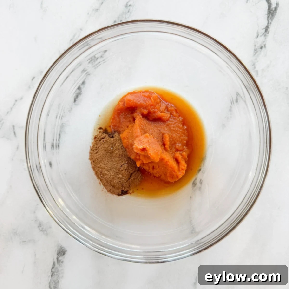 Bowl with pumpkin, maple syrup, vanilla, spices, and salt ready to be whisked.
