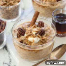 Pumpkin spice overnight oats in a glass serving bowl with cinnamon, pecans, maple syrup, and spoon.