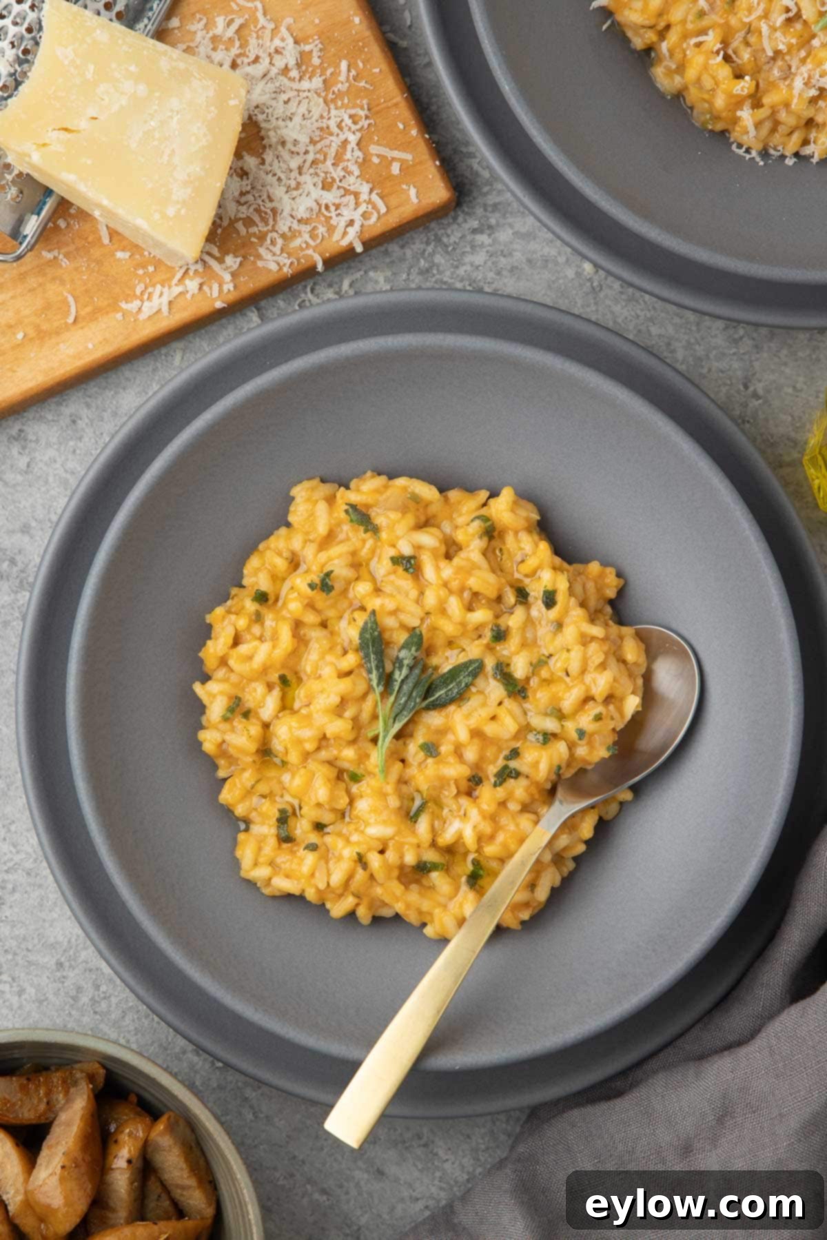A gray bowl of creamy orange pumpkin risotto with fried sage leaves. 