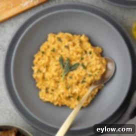 A gray bowl of pumpkin risotto with a golden spoon and sage leaves.