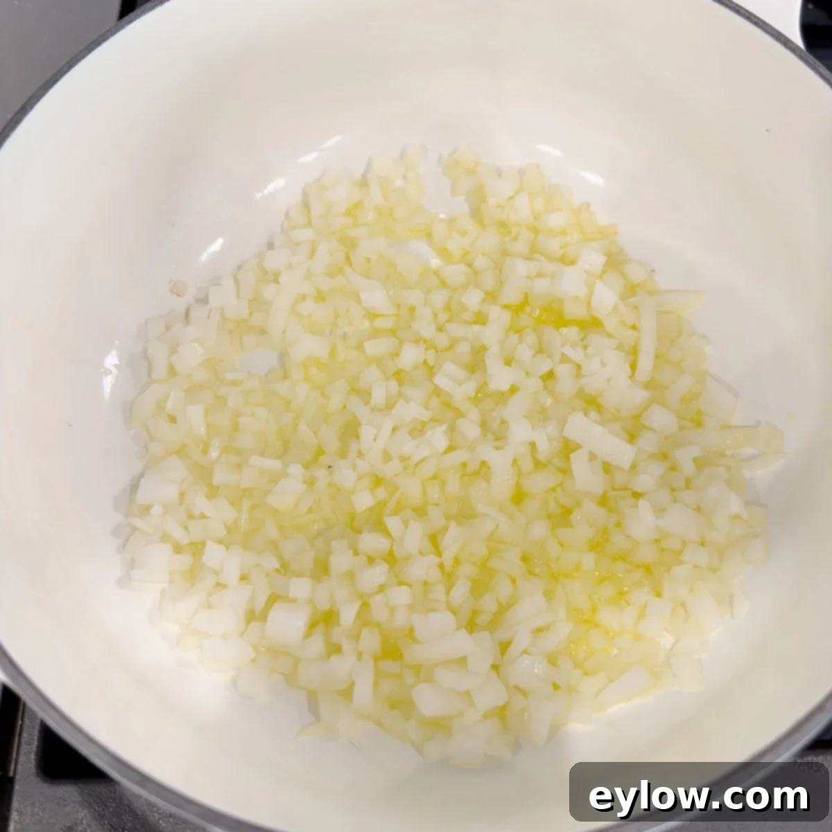 Sautéing onion in olive oil in a white pan.