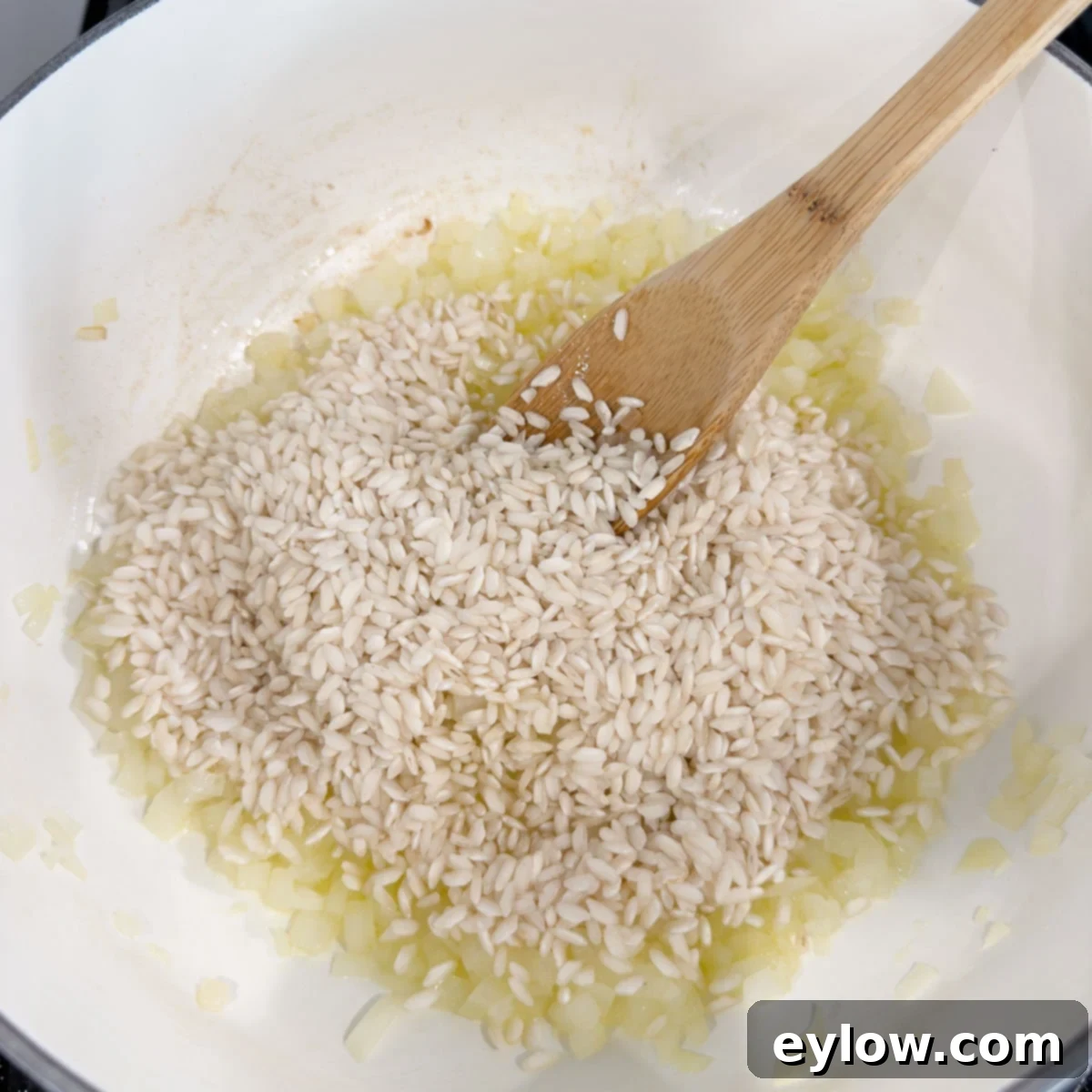 Rice, onions, and oil in a pot to make risotto, with a wooden spoon.
