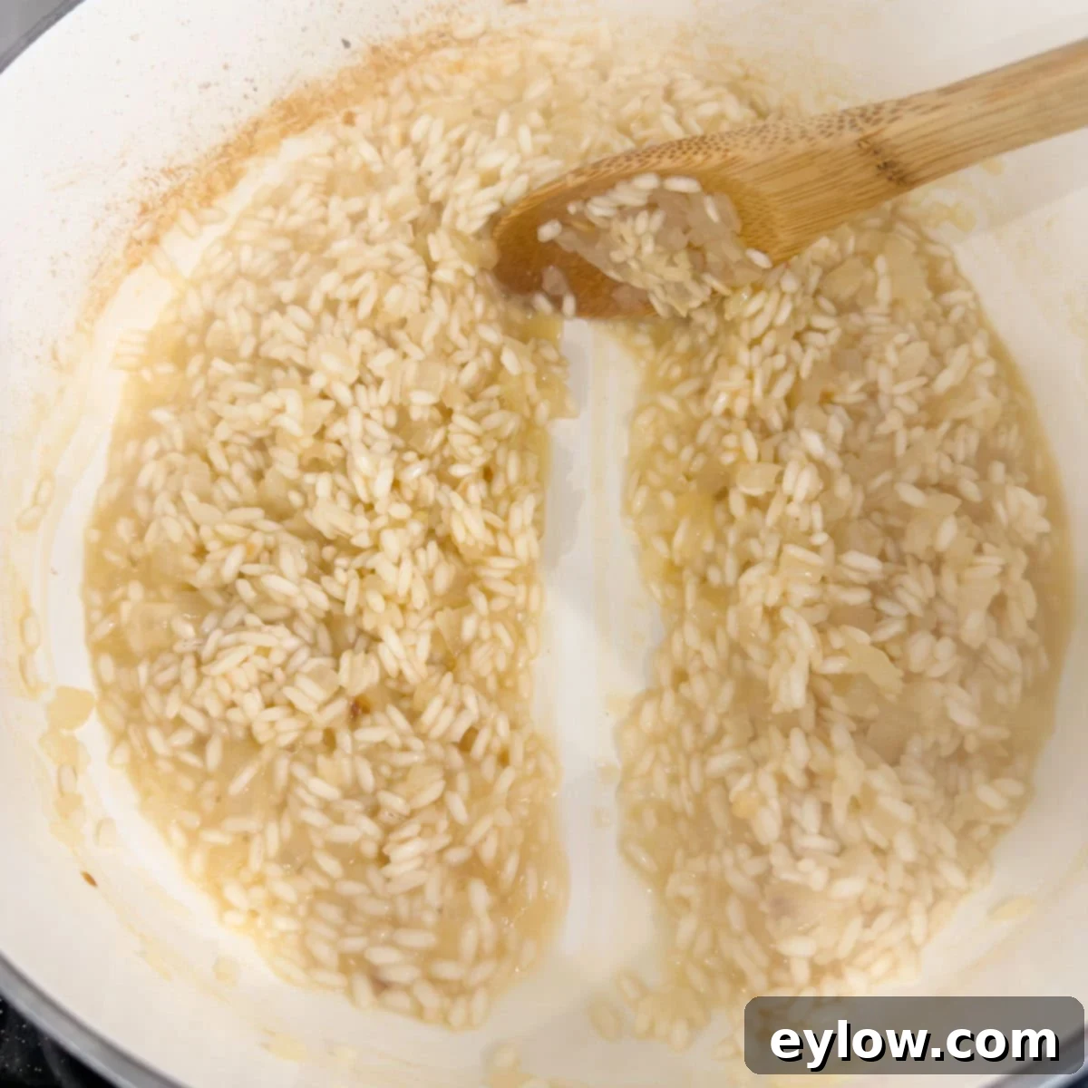 Wooden sppon drawing aline through cooking rice to show it is ready for more broth.