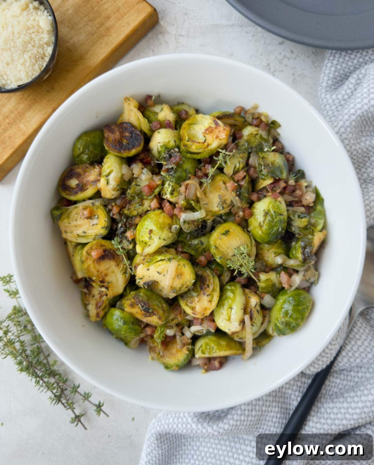 Golden Brussels Sprouts with Crispy Pancetta 2 A white bowl brimming with perfectly cooked Brussels sprouts, golden-brown and tender, adorned with crisp pancetta bits, fresh herbs, and translucent shallots. The dish exudes warmth and inviting aroma.