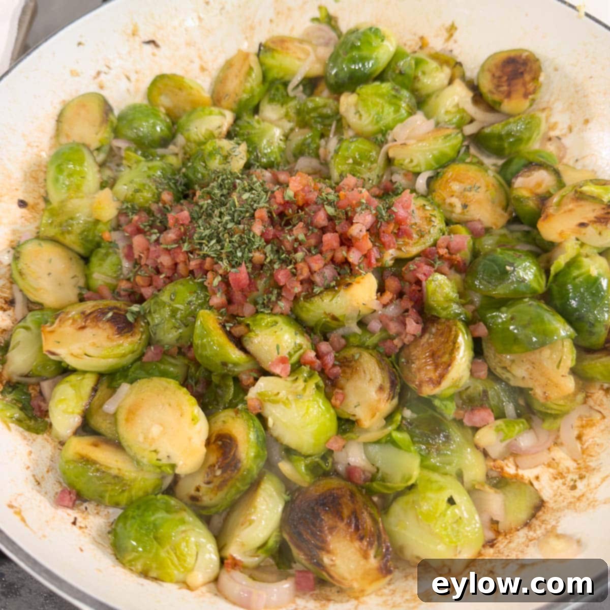 Golden Brussels Sprouts with Crispy Pancetta 11 A close-up of a pan filled with beautifully cooked Brussels sprouts, mixed with crispy pancetta and fresh green herbs, glistening with a light glaze, ready to be served.