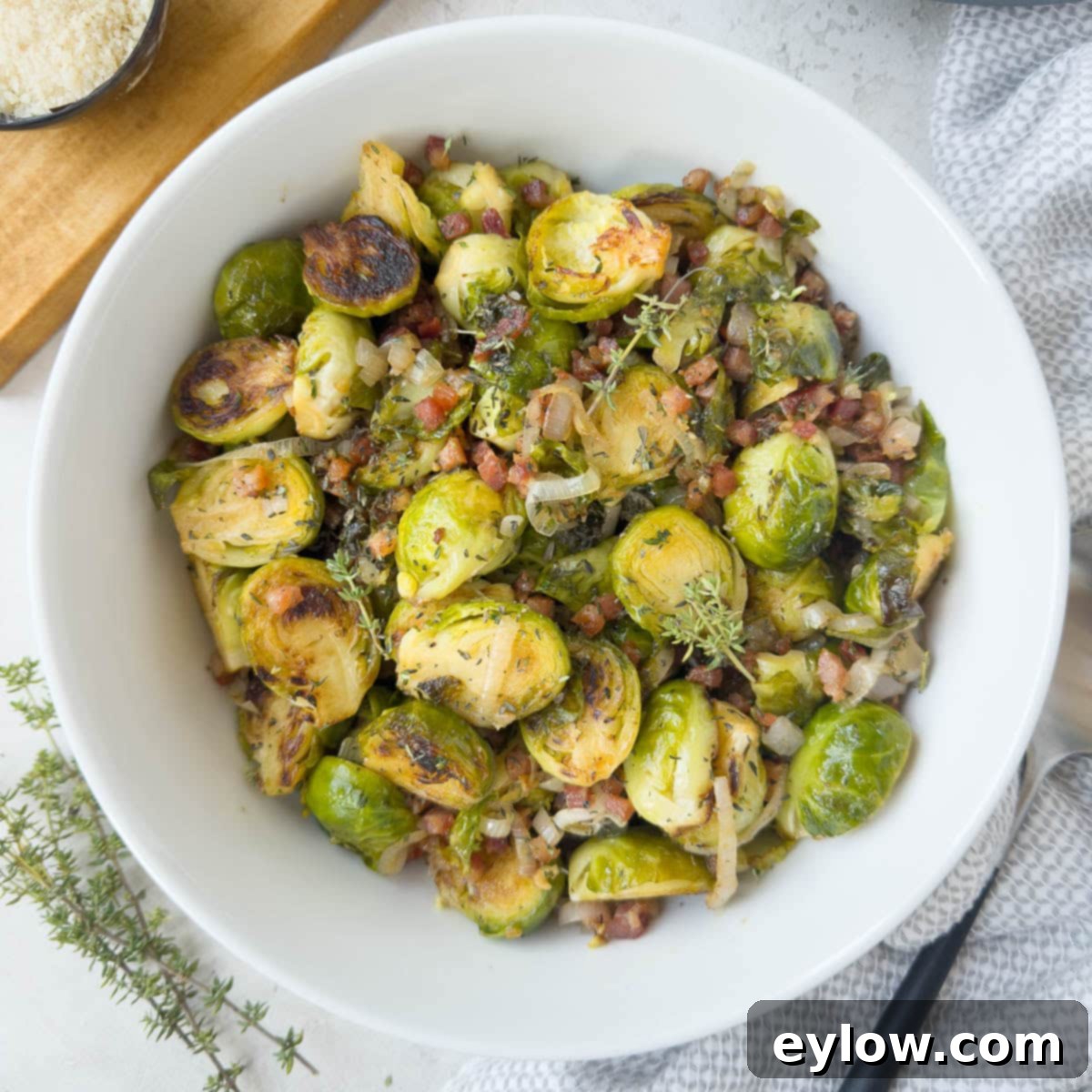 Golden Brussels Sprouts with Crispy Pancetta 12 A beautifully presented round bowl of golden-green Brussels sprouts, richly adorned with crispy pancetta, aromatic herbs, and sweet shallots, ready for serving at a festive meal.