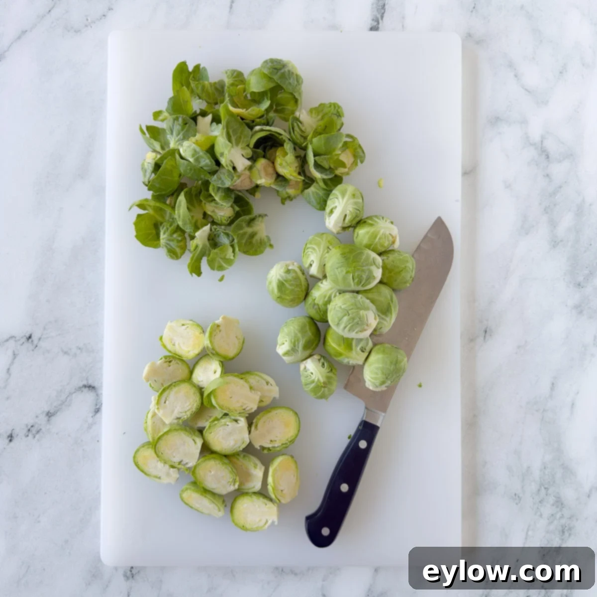 Golden Brussels Sprouts with Crispy Pancetta 4 A close-up shot of hands trimming the root ends and removing outer leaves of fresh Brussels sprouts, preparing them for cooking. The sprouts are halved, showcasing their inner layers.
