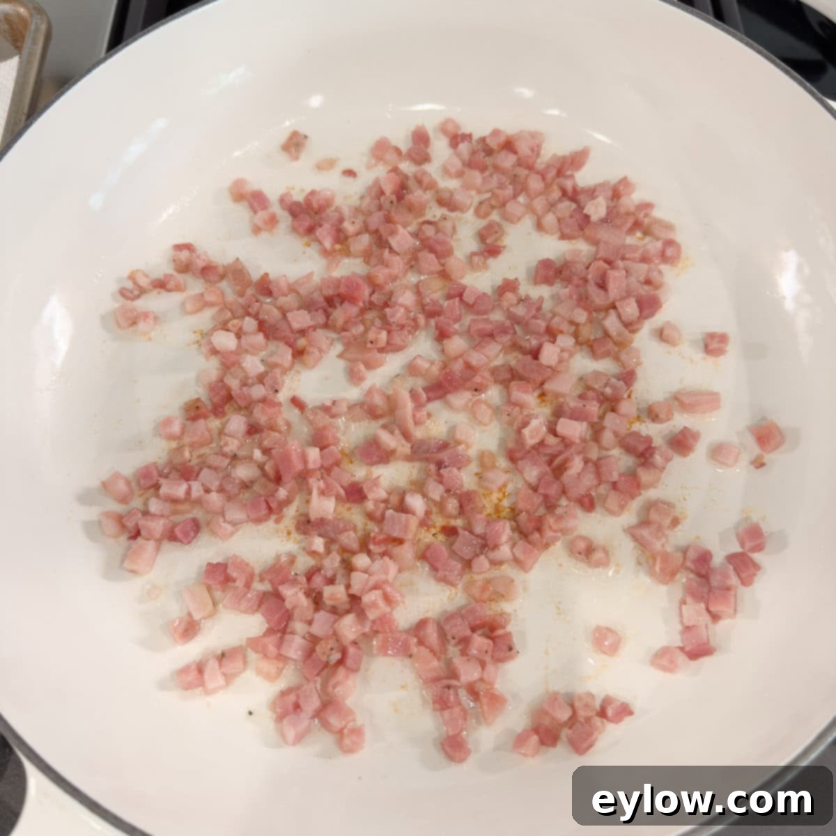 Golden Brussels Sprouts with Crispy Pancetta 5 Diced pancetta browning and sizzling in a wide, shallow pan on a stovetop, releasing its fat and turning golden crisp. The pan shows signs of flavorful fond forming at the bottom.