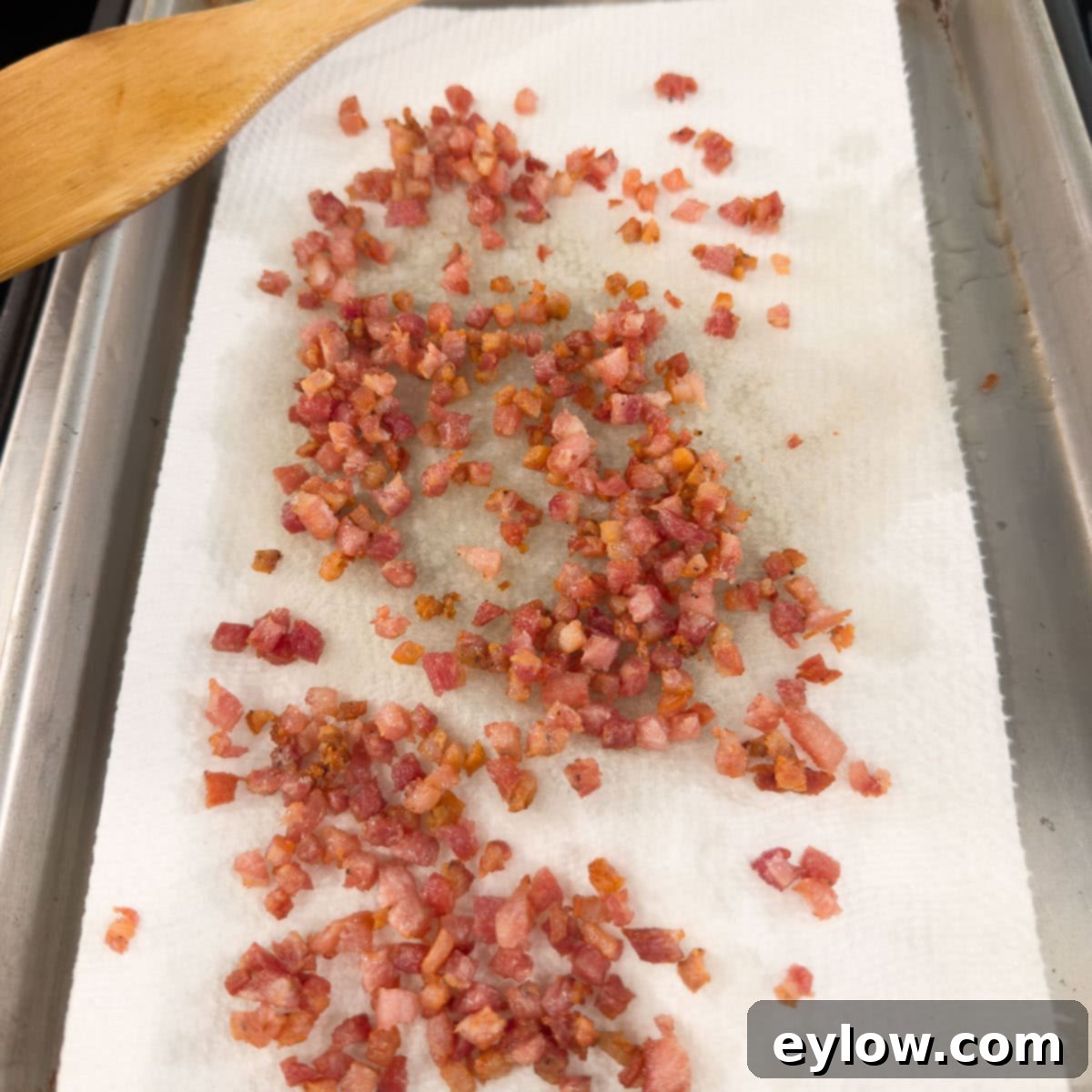 Golden Brussels Sprouts with Crispy Pancetta 6 A slotted spoon carefully removes crispy, browned pancetta pieces from a pan, placing them onto a plate lined with paper towels to drain excess fat, leaving behind a rich, flavorful residue in the pan.