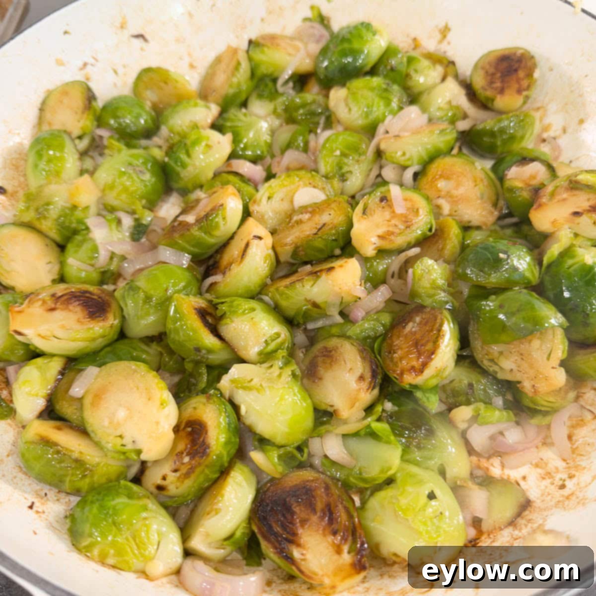 Golden Brussels Sprouts with Crispy Pancetta 9 Perfectly browned Brussels sprouts mixed with translucent pink shallots and minced garlic, gently cooking in a pan on the stovetop, releasing fragrant aromas.